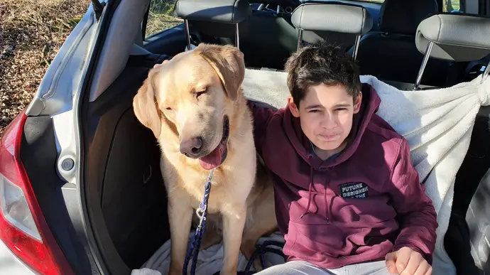 Ein Junge sitzt mit seinem Hund im Kofferraum eines Autos und lächelt in die Kamera