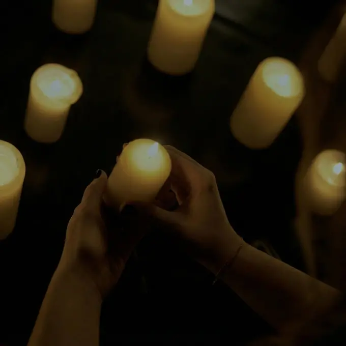 Hände halten eine brennende Kerze in dunkler Umgebung