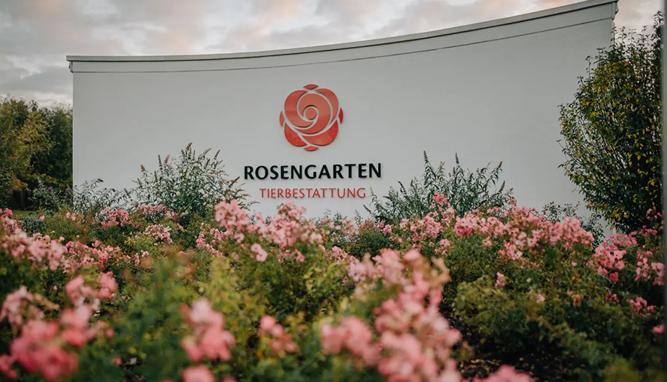 Das Bild zeigt den Eingang eines Tierkrematoriums mit dem Logo "Rosengarten" und einem gepflegten Rosengarten.