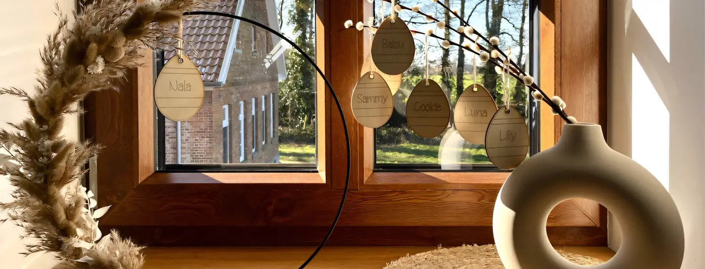 Fensterbank mit einem dekorativen Kranz, einer Vase und Namensplaketten von Haustieren wie 'Nala', 'Balou' und 'Luna'