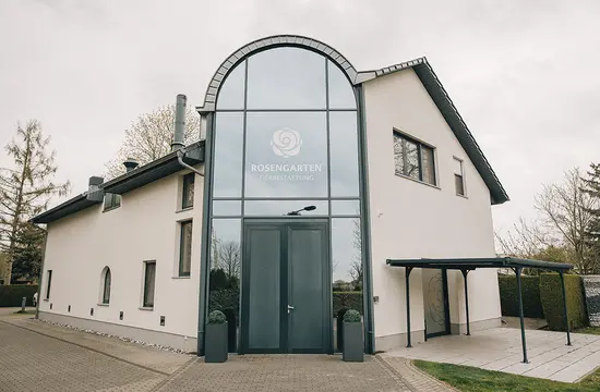 Das Bild zeigt einen gepflegten Außenbereich mit einem zentralen Baum und symmetrischen Pflanzen in Töpfen, die den Weg umrahmen.
