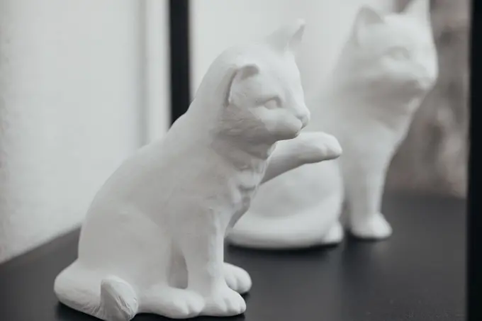 Weiße Katzenfigur aus Keramik mit erhobener Pfote auf dunkler Oberfläche