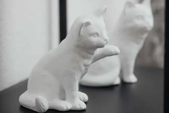 Weiße Katzenfigur aus Keramik mit erhobener Pfote auf dunkler Oberfläche