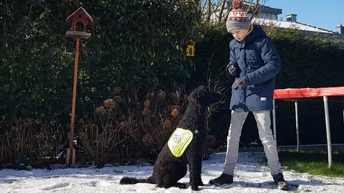 Ein Junge spielt mit seinem Assistenzhund im Schnee.