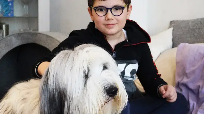 Ein Junge sitzt auf dem Sofa und streichelt seinen flauschigen Hund, der entspannt und ruhig wirkt.