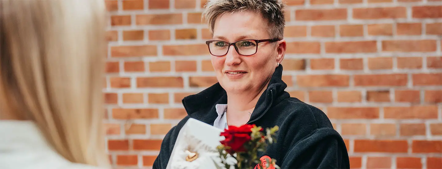 Eine Mitarbeiterin übergibt einer Person eine Box mit einer Rose und einer Urne