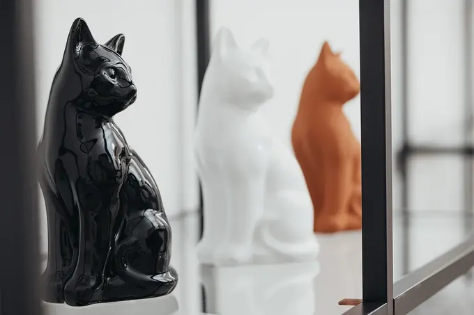 Dekorative Katzenurnen aus Keramik in Schwarz, Weiß und Terrakotta auf einem Regal
