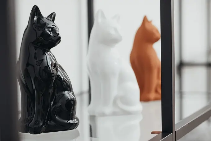 Dekorative Katzenurnen aus Keramik in Schwarz, Weiß und Terrakotta auf einem Regal