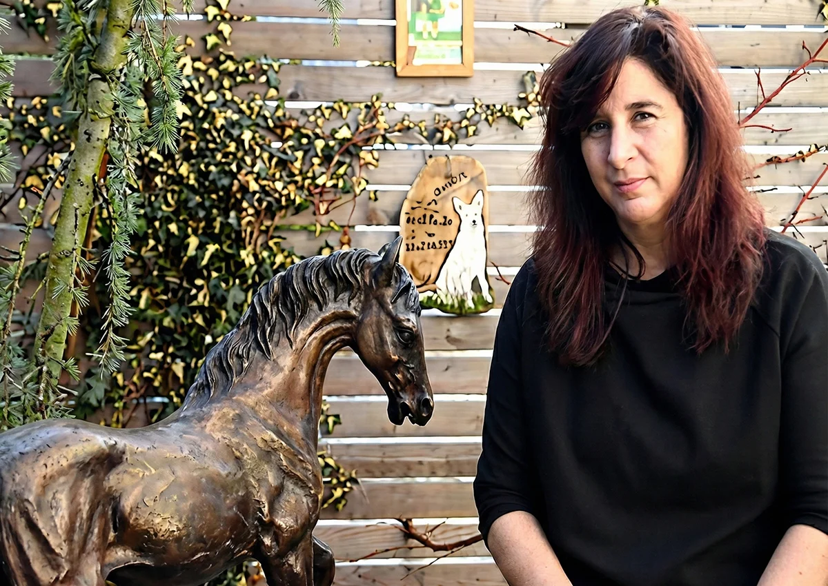 Frau sitzt im Garten neben einer Pferdeskulptur aus Metall