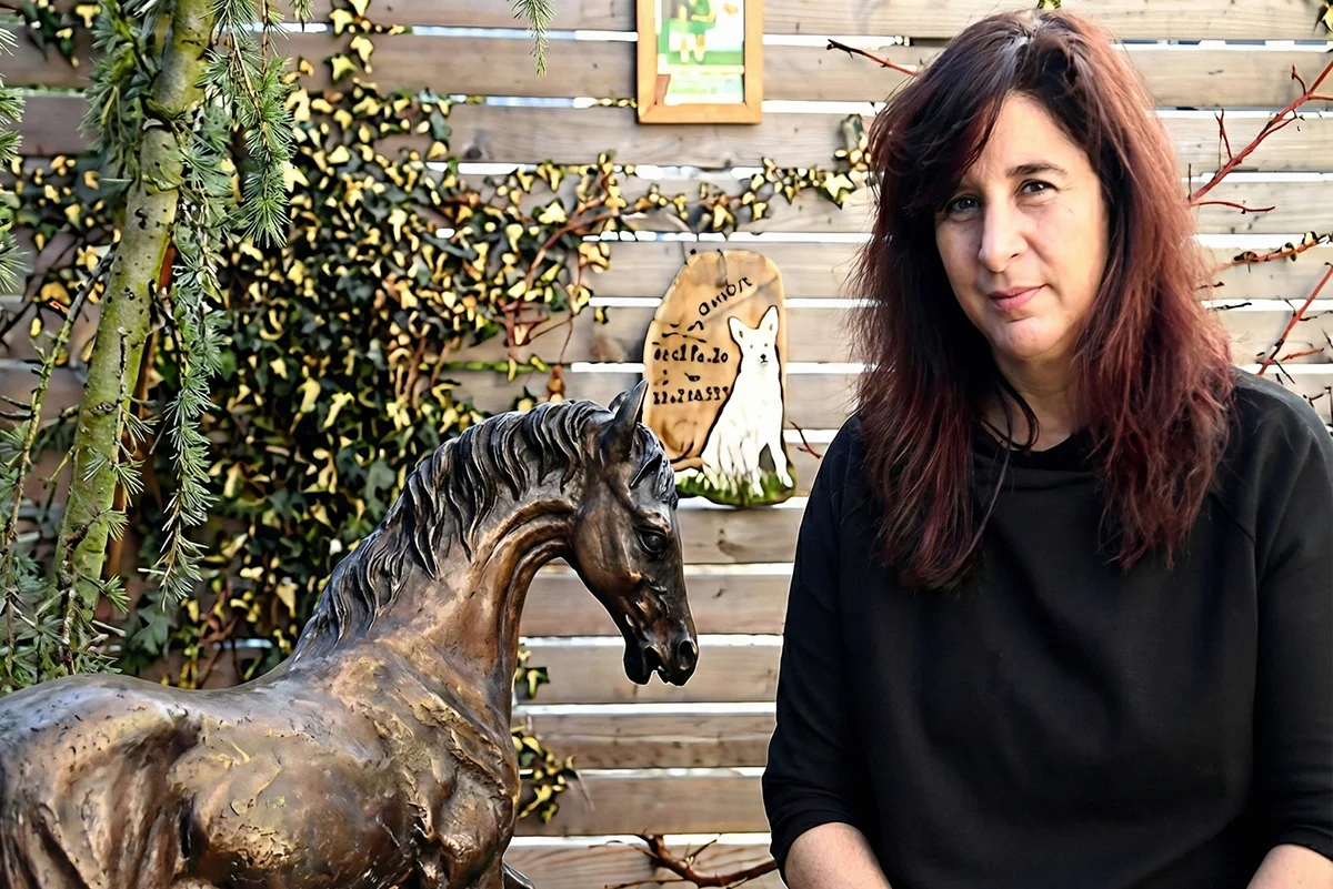 Frau sitzt im Garten neben einer Pferdeskulptur aus Metall
