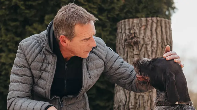 Älterer Mann streichelt liebevoll seinen Hund und blickt ihm draußen in natürlicher Umgebung in die Augen