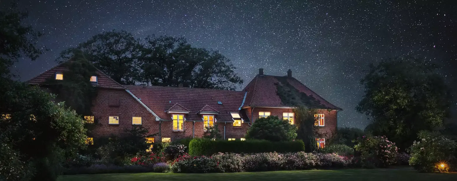 Beleuchtetes Gebäude inmitten eines blühenden Gartens unter sternenklarem Nachthimmel – ein Ort der Ruhe, Erinnerung und Verbundenheit … im ROSENGARTEN-Tierkrematorium