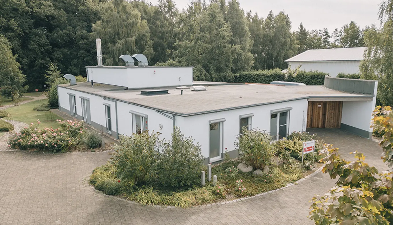 Das Bild zeigt einen Garten mit einem geschwungenen Kiesweg, der von einem Eisenbogen überspannt wird.