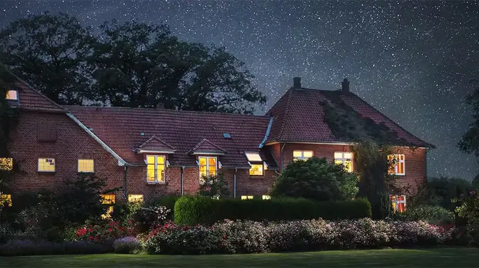 Beleuchtetes Gebäude inmitten eines blühenden Gartens unter sternenklarem Nachthimmel – ein Ort der Ruhe, Erinnerung und Verbundenheit … im ROSENGARTEN-Tierkrematorium