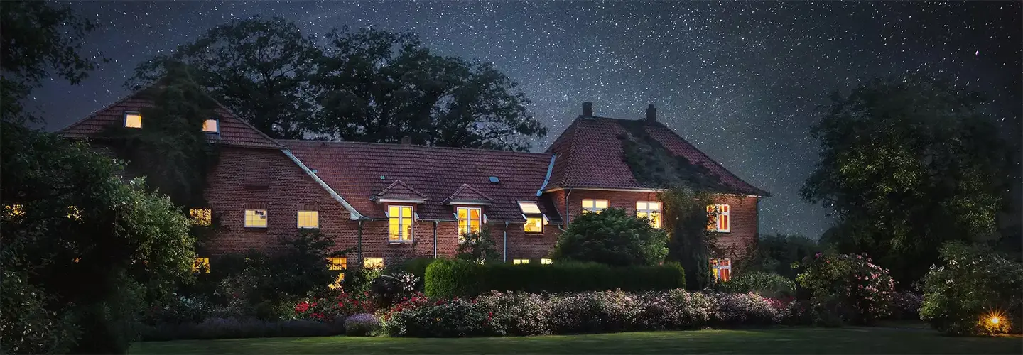 Beleuchtetes Gebäude inmitten eines blühenden Gartens unter sternenklarem Nachthimmel – ein Ort der Ruhe, Erinnerung und Verbundenheit … im ROSENGARTEN-Tierkrematorium