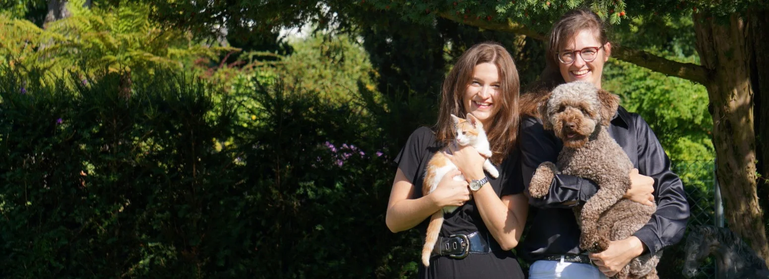 Zwei Personen stehen im Garten und halten eine Katze und einen Hund im Arm