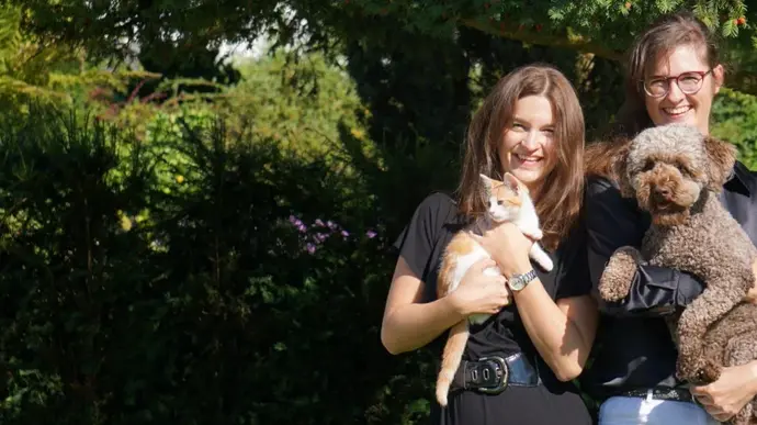 Zwei Personen stehen im Garten und halten eine Katze und einen Hund im Arm