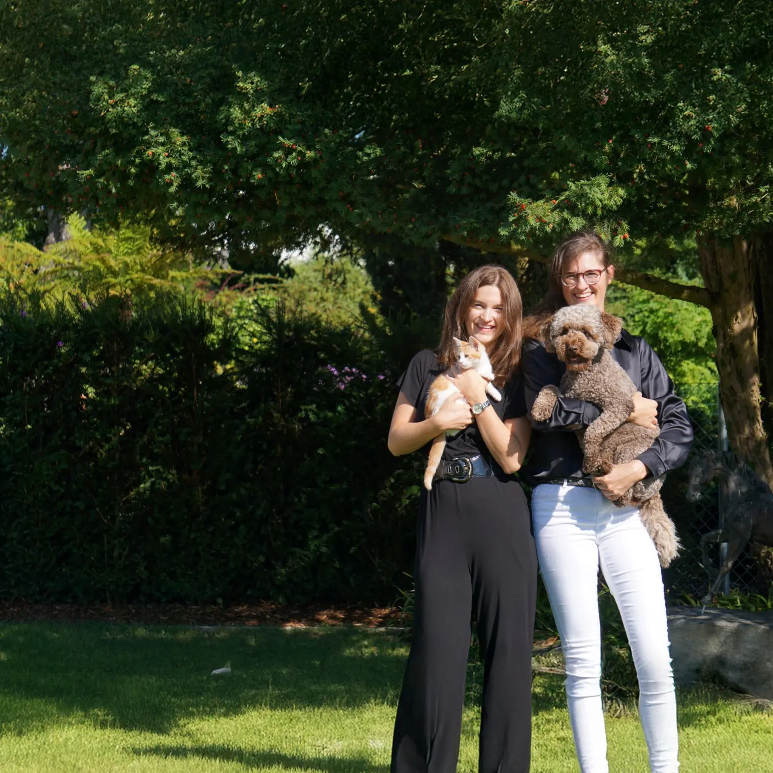 Zwei Personen stehen im Garten und halten eine Katze und einen Hund im Arm