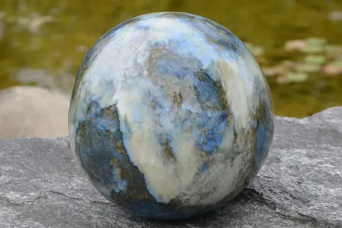 Runde Urne aus Stein liegt auf einem Felsen am Wasser