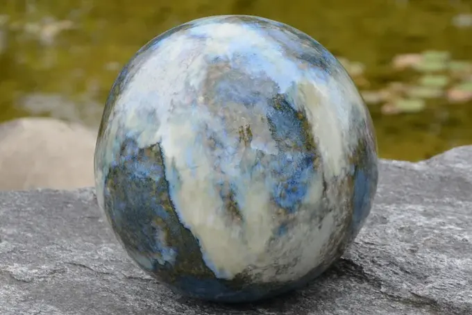 Runde Urne aus Stein liegt auf einem Felsen am Wasser