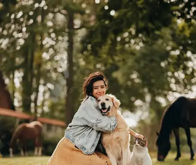 Das Bild zeigt eine Frau, die glücklich ihren Hund streichelt. Der Hund, ein Golden Retriever, sitzt ruhig neben ihr, beide wirken entspannt und freundlich.