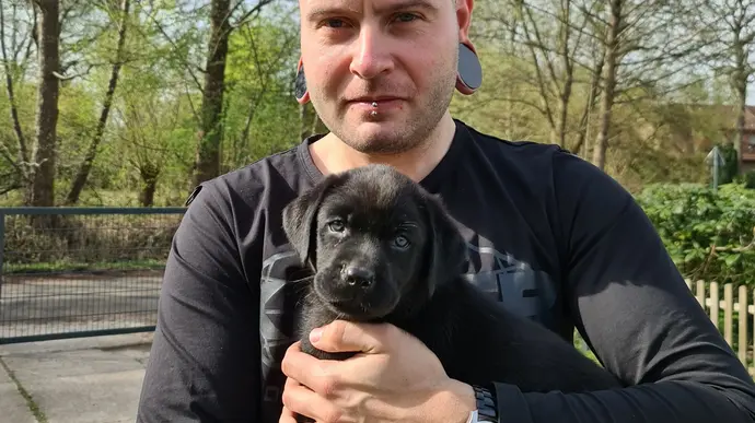 Ein Mann hält einen schwarzen Welpen in den Armen. 