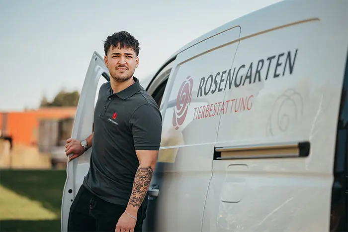 Ein Mitarbeiter der ROSENGARTEN-Tierbestattung steht an der geöffneten Tür eines weißen Transportfahrzeugs mit Firmenlogo